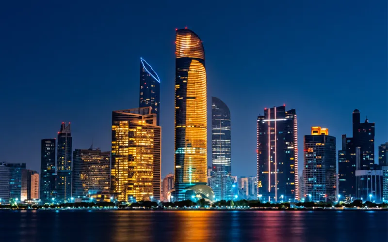City skyline at night with glowing high-rise towers reflected in the water